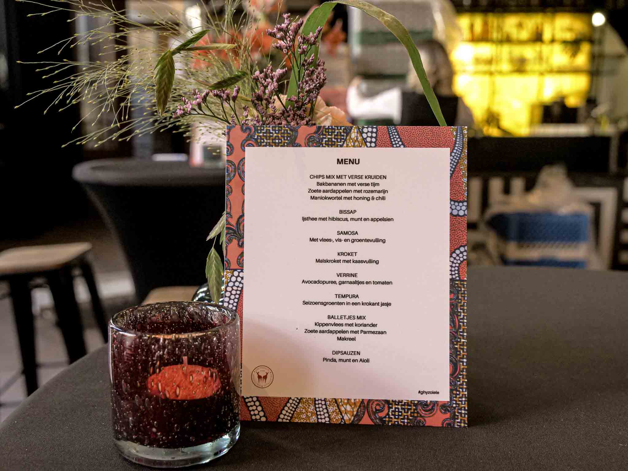 Menu met een kaarsje en bar met medewerkster op de achtergrond.