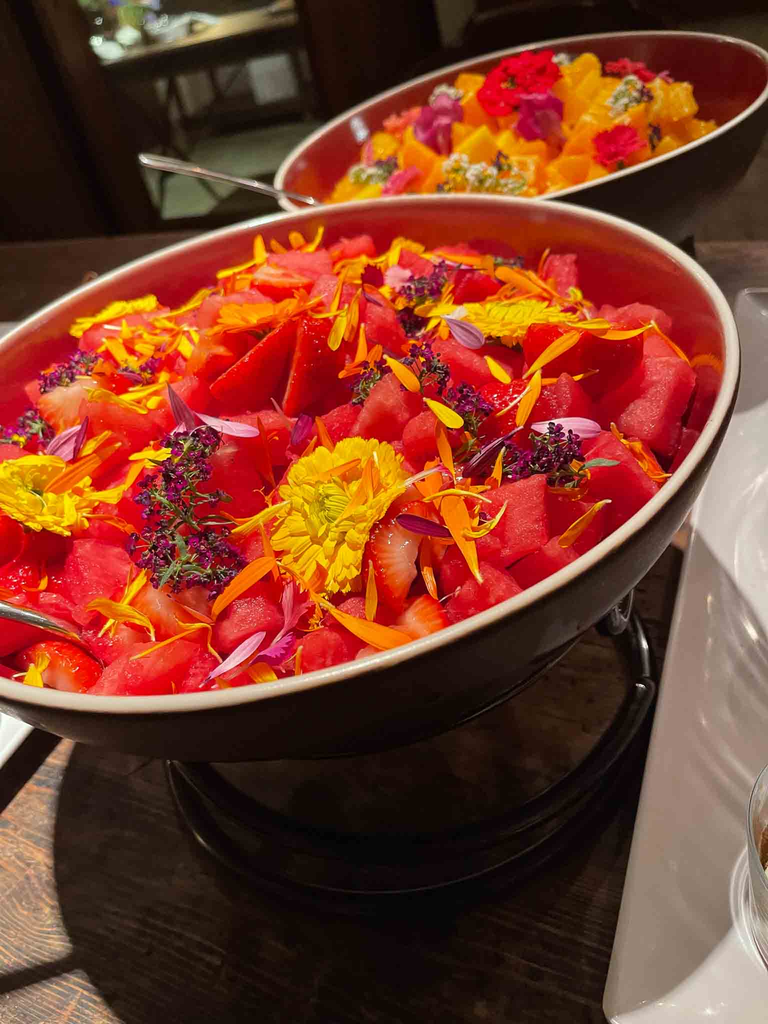 2 zilveren schalen van een rode zomersalade met eetbare bloemen, aardbei en watermeloen.