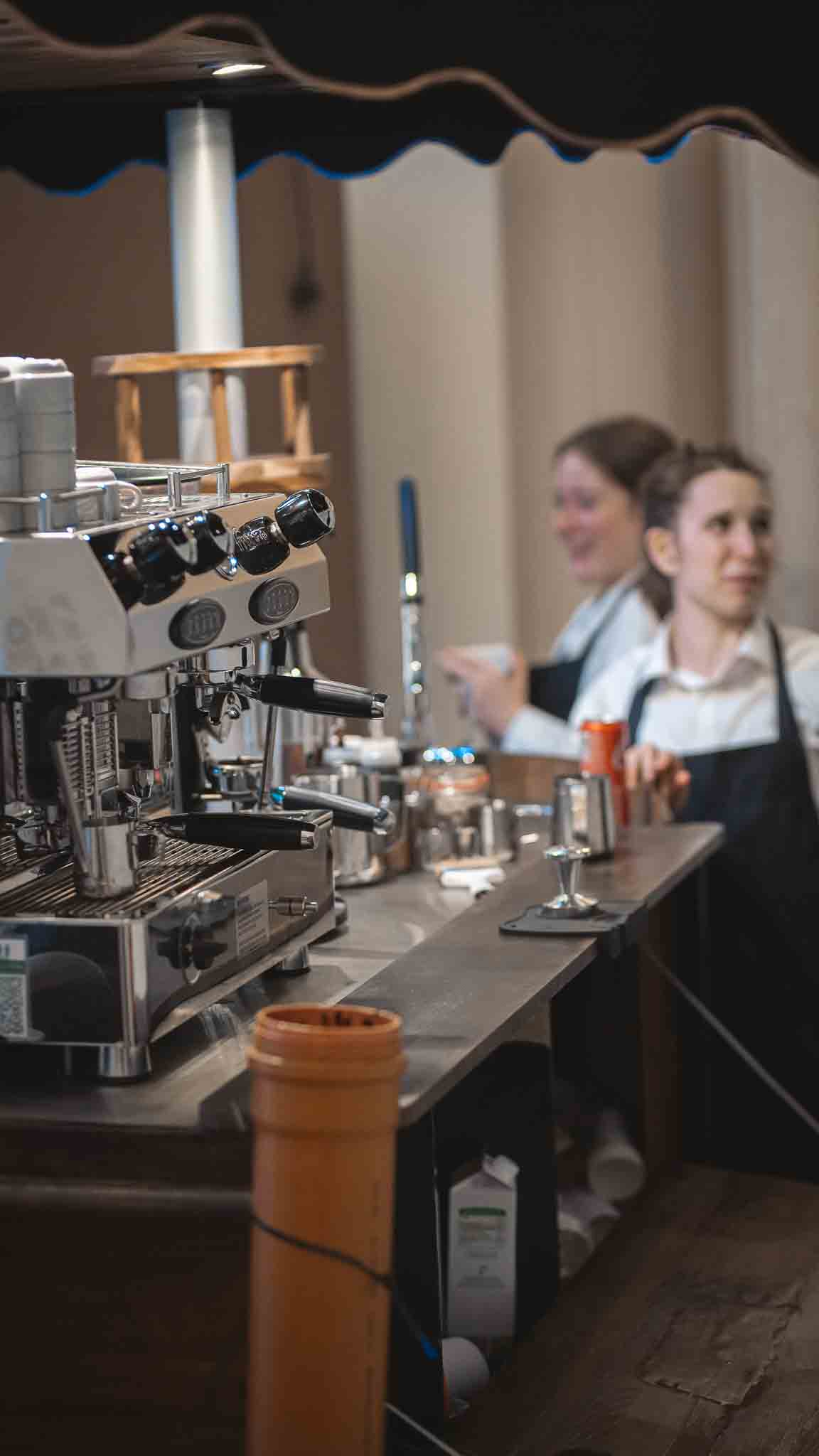 Koffiemachine met 2 serveersters in de achtergrond.