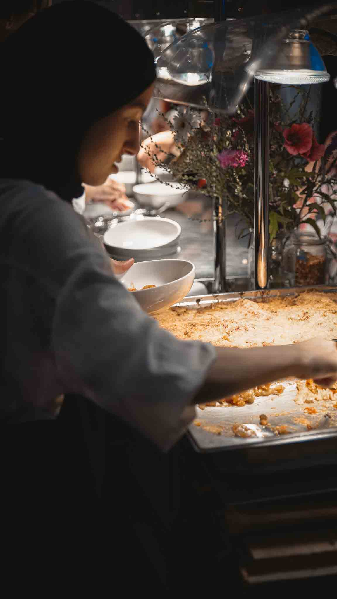 Medewerkster schept eten in wit kommetje.