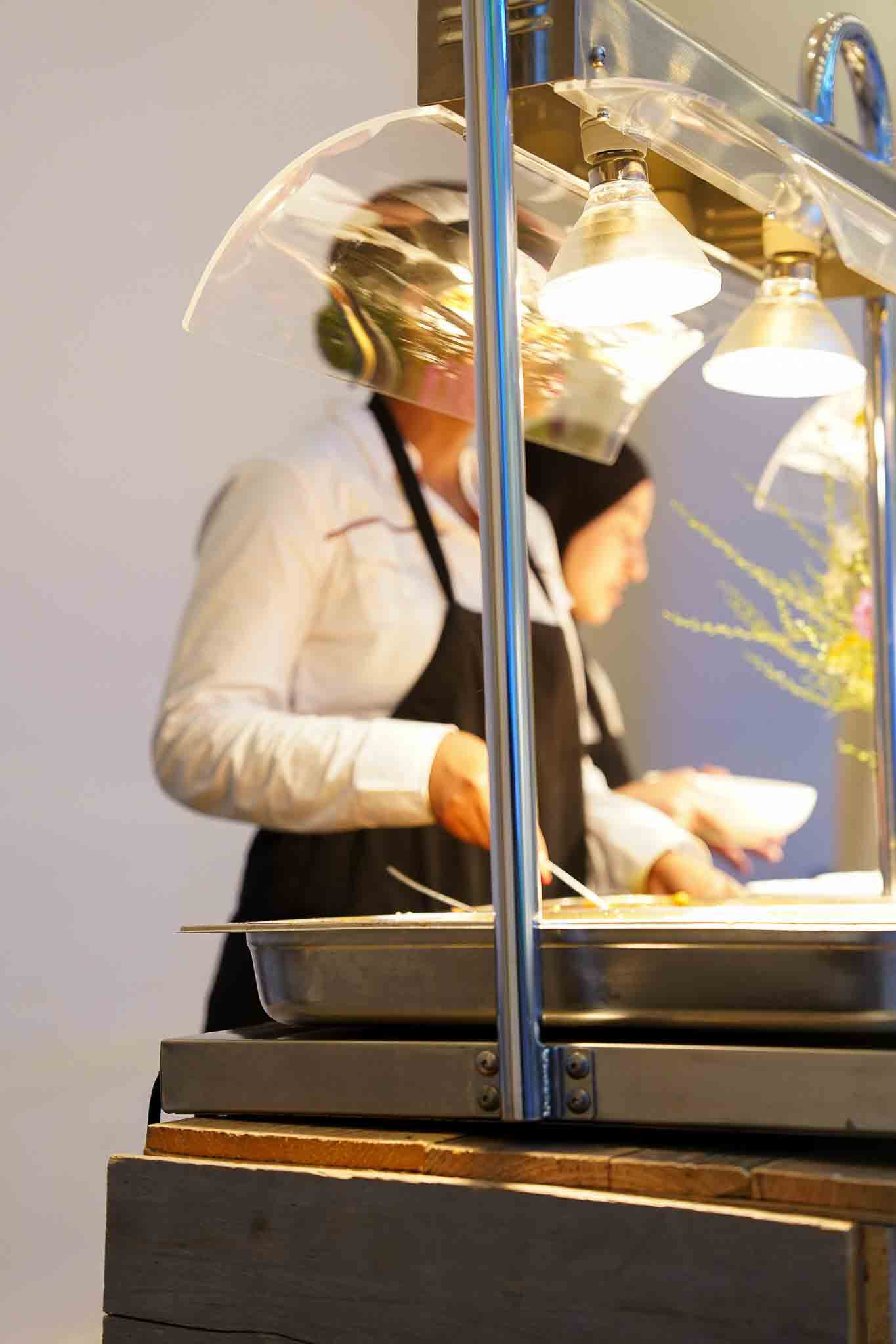 Medewerksters scheppen eten in witte kommetjes met mooie belichting van lichtjes.