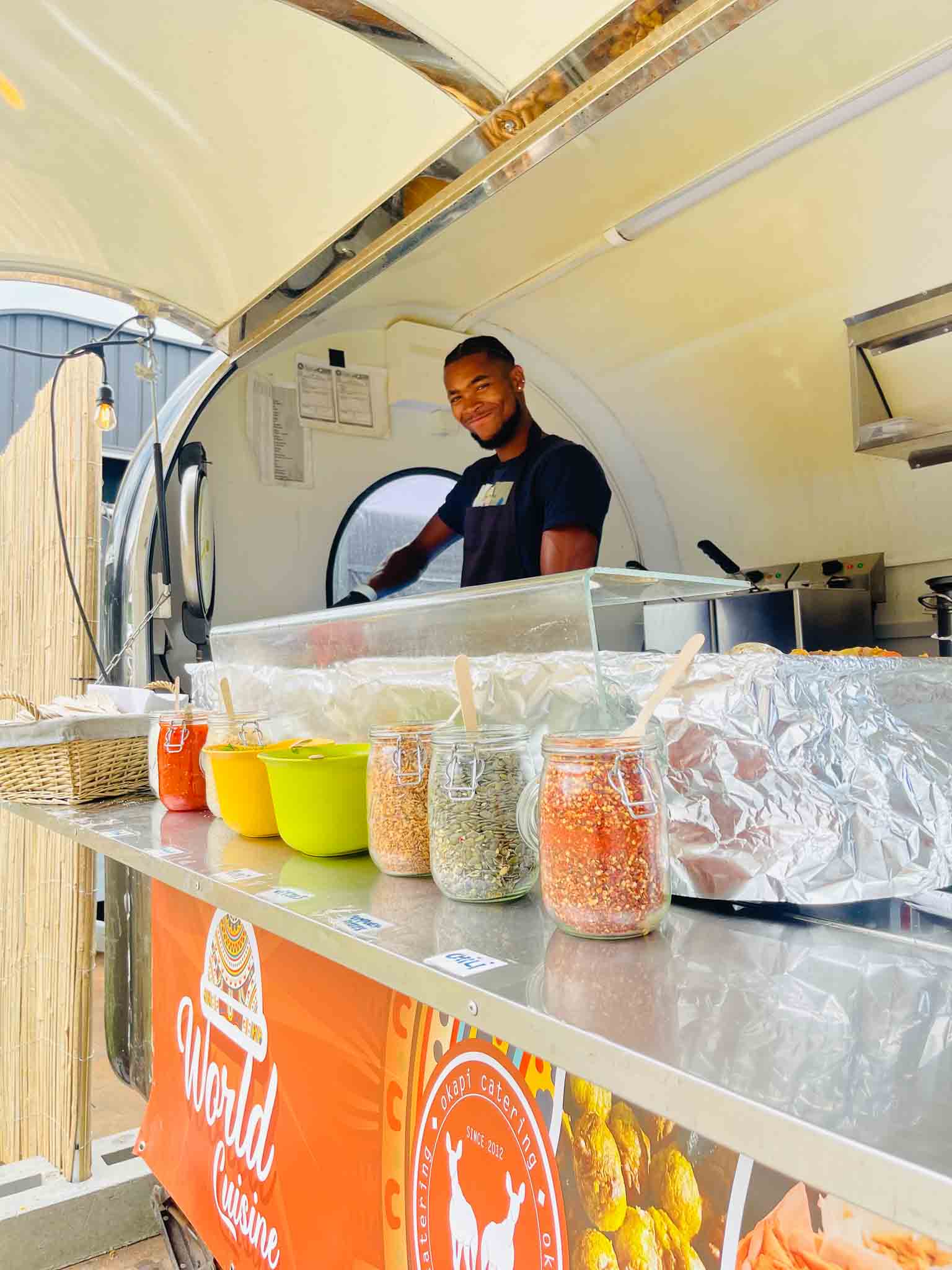 Een medewerker staat glimlachend in een foodtruck klaar om klanten te serveren.